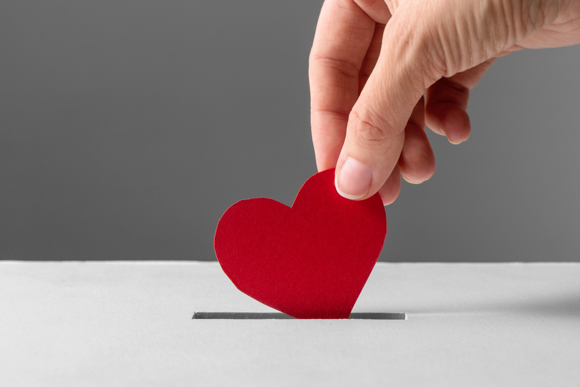 Hand Putting Red Heart into Donation Box